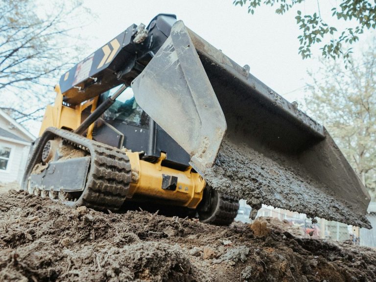 Baggerarbeiten für Drainage und Entwässerung rund ums Gebäude Gelber Kompaktbagger beim Ausheben von Erdreich für Entwässerungssystem – BriqWerk Bauunternehmen Bochum
